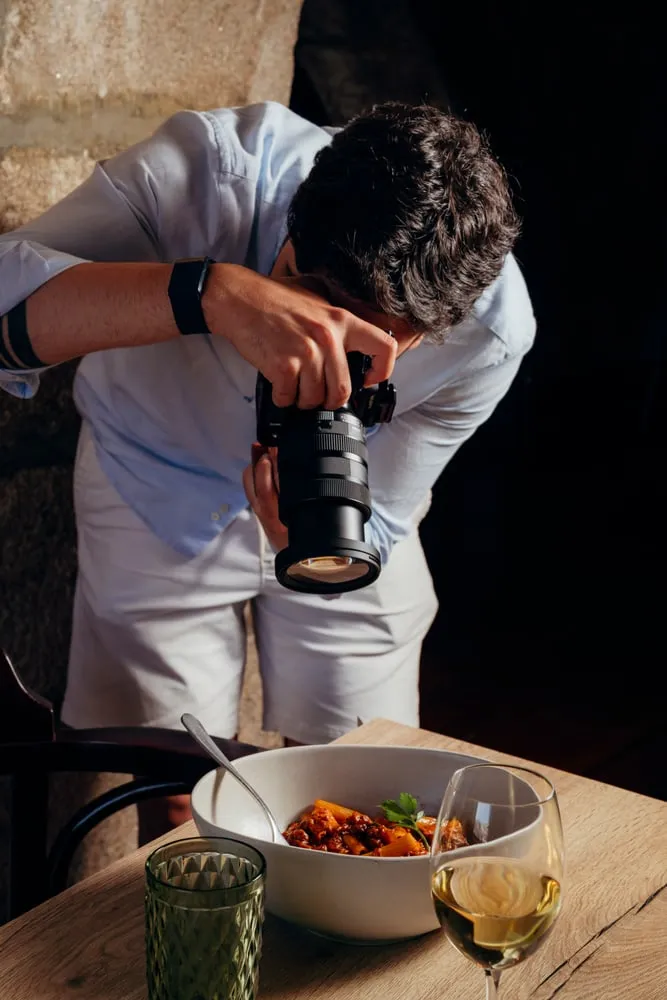 O fotógrafo debruçado sobre um prato e um copo de vinho