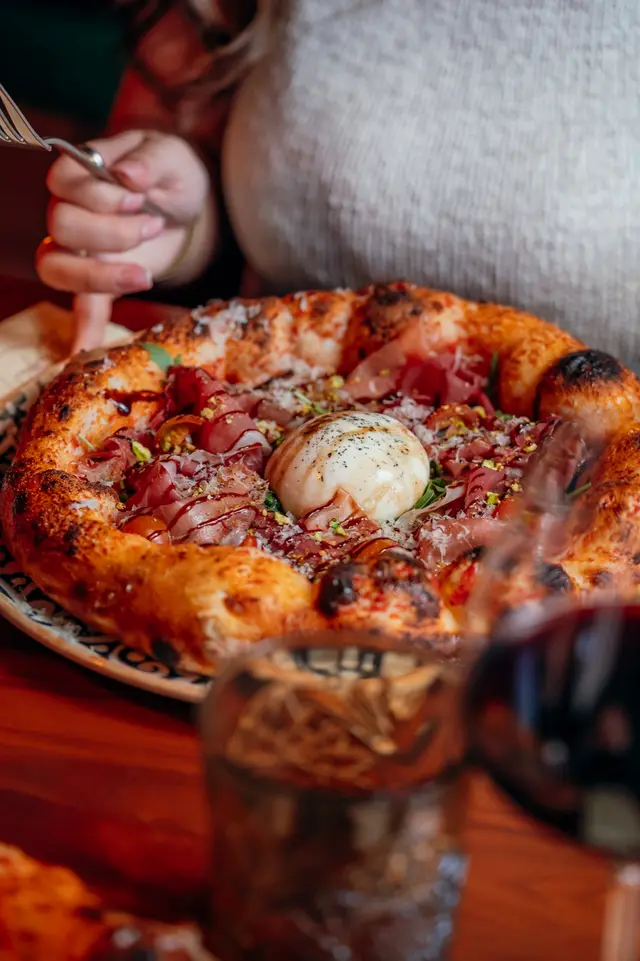 Pizza com burrata, presunto e pistácio, com uma cliente à mesa
