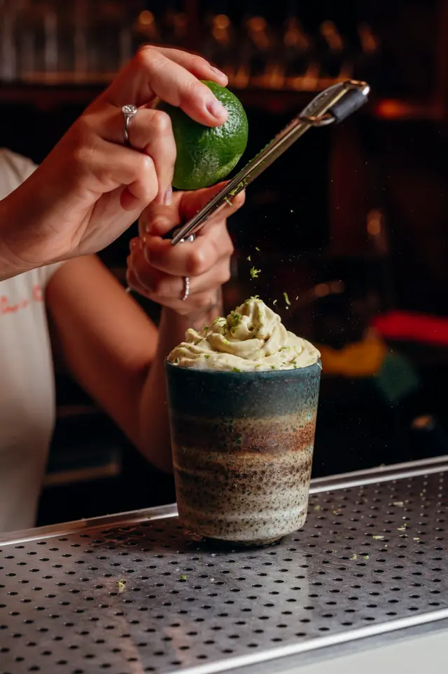 Mãos a raspar casca de lima sobre um cocktail